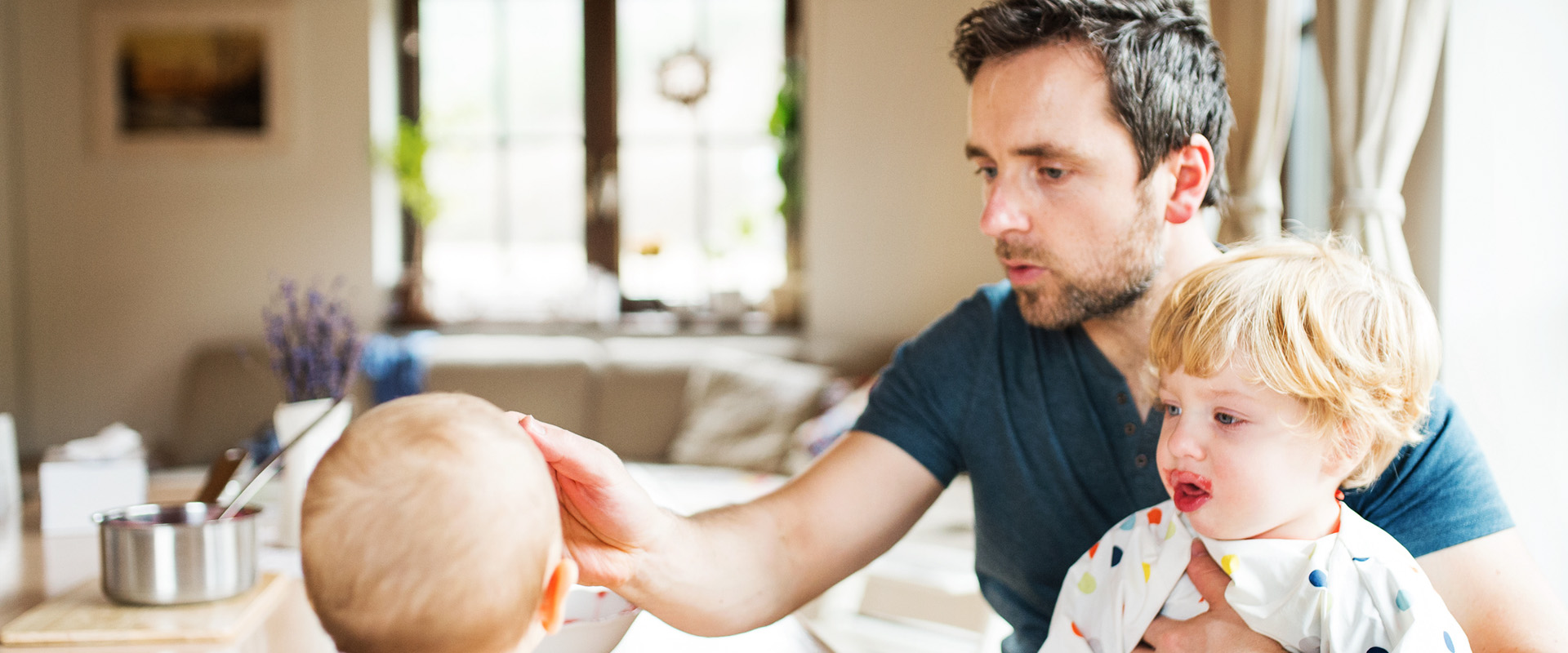 bild zeigt ein vater am mittagstisch, zwei kinder am füttern